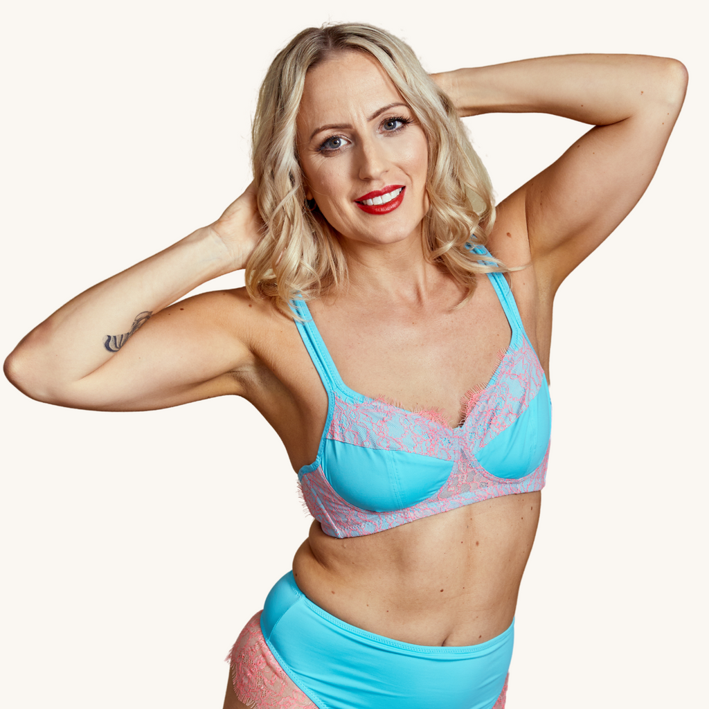 A smiling blond woman wears our Maestra blue full cup bra with blush pink lace details - Valiant Lingerie